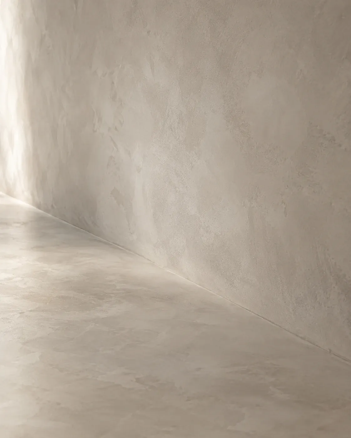 Junction of a light microcement wall and floor, cloudy texture in side light
